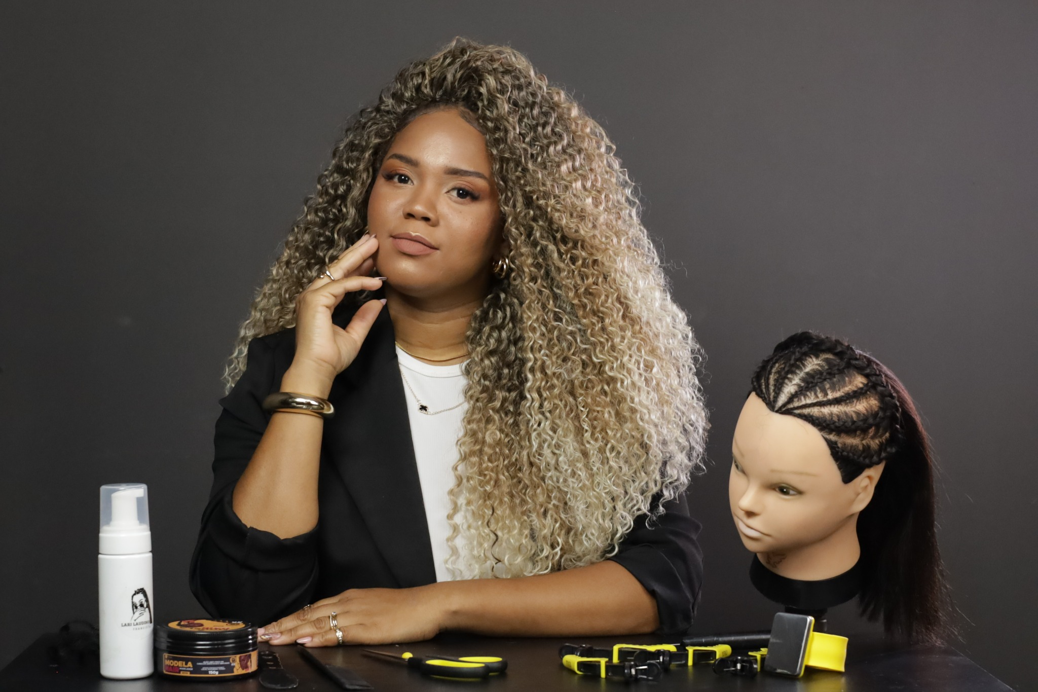 Larissa com materiais de tranças e uma cabeça de treino